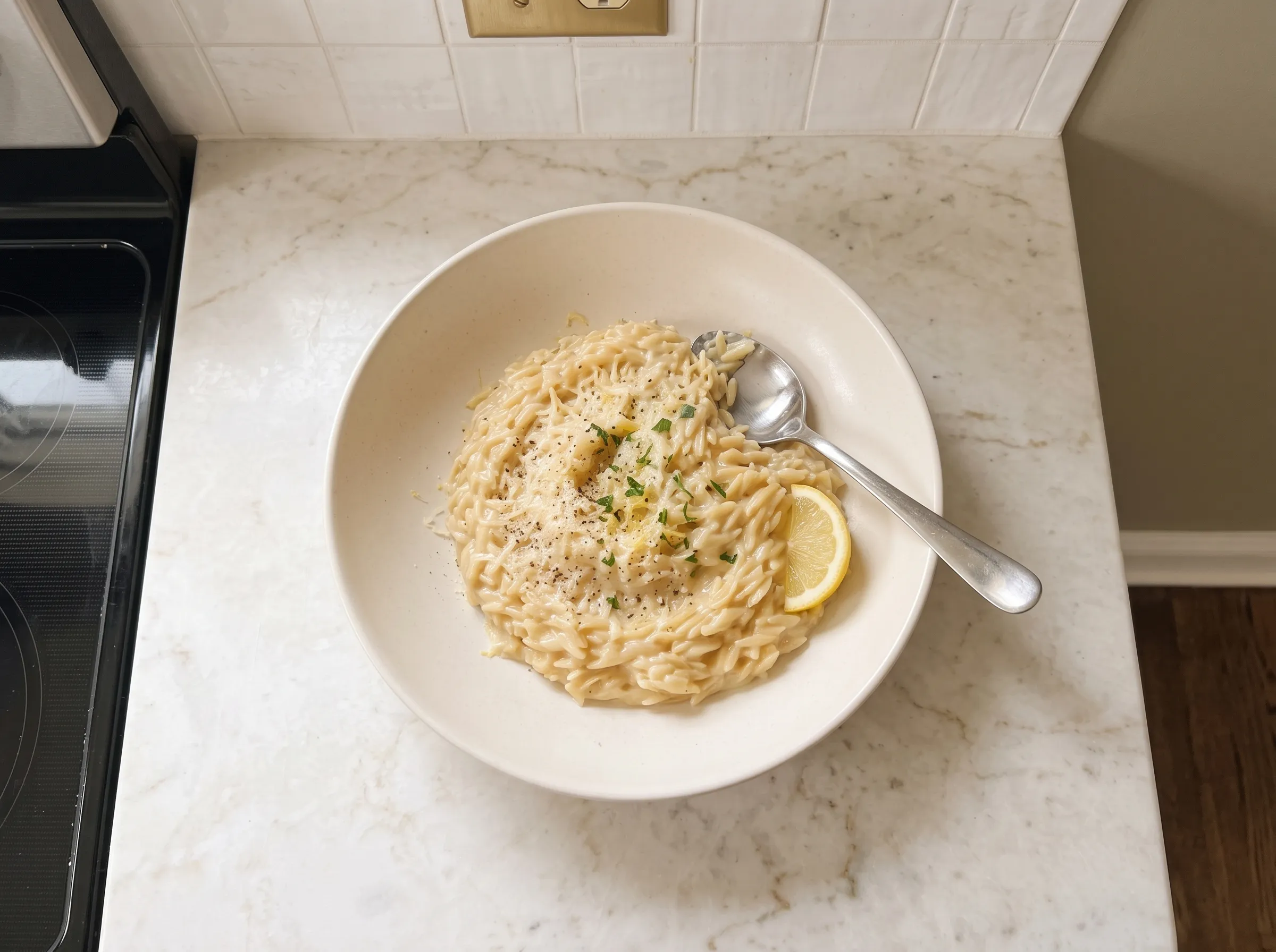 Creamy lemon orzo with a sprinkle of cheese, served in a white bowl with parsley and lemon slices.