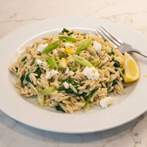 one-pan-orzo-with-spinach-and-feta: Orzo with spinach, scallions, and feta, garnished with lemon, served on a white plate.