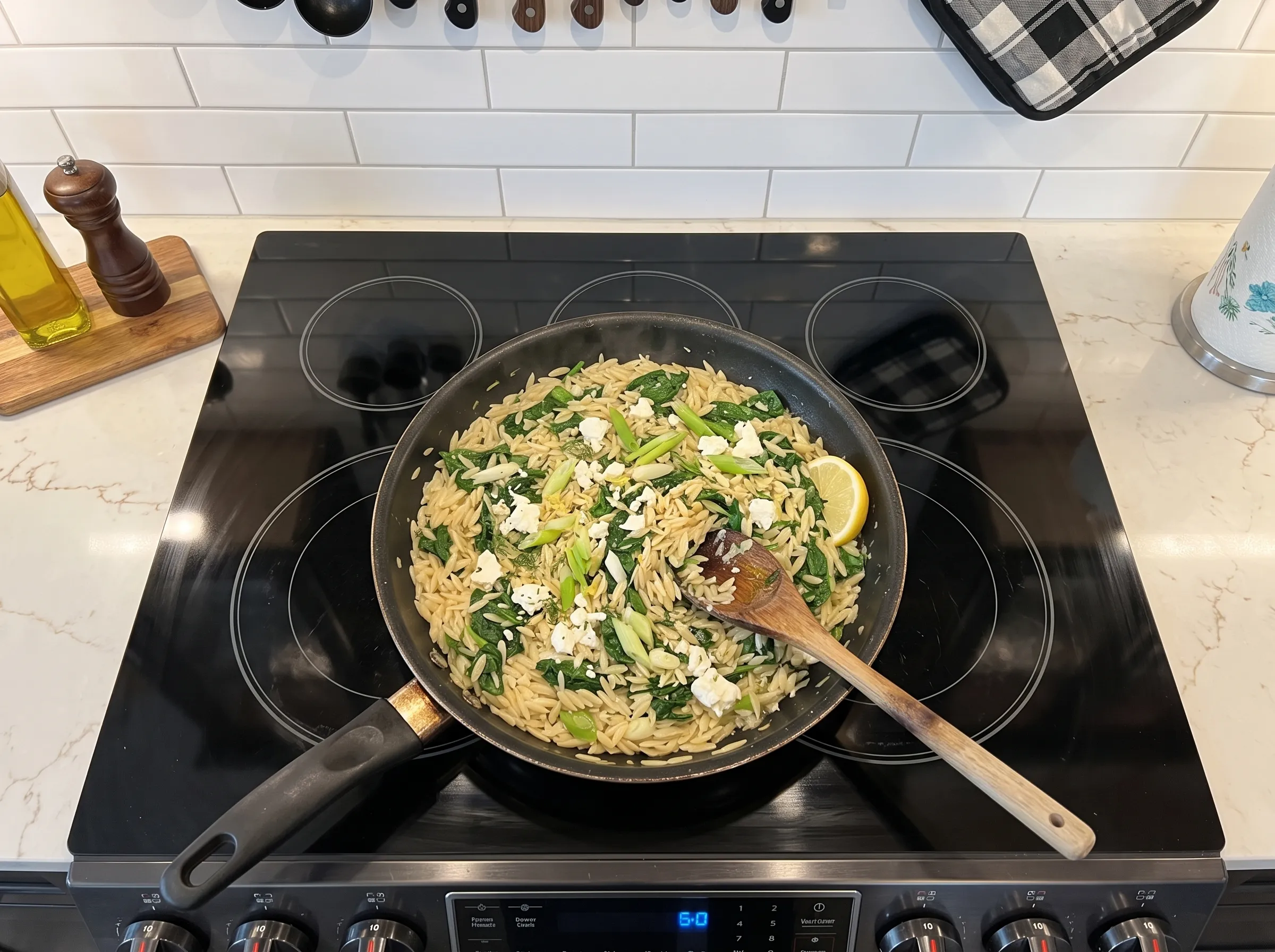 Lemon orzo with spinach and feta, sautéed in a black skillet with a wooden spoon and lemon wedge garnish.
